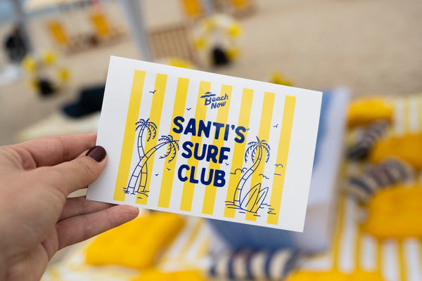 A hand holding a custom Beach Now party invitation showing the text 